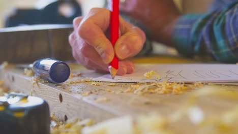 Primer-Plano-De-Un-Carpintero-De-Sexo-Masculino-Senior-En-Un-Taller-De-Garaje-Esbozando-El-Diseño-En-Papel