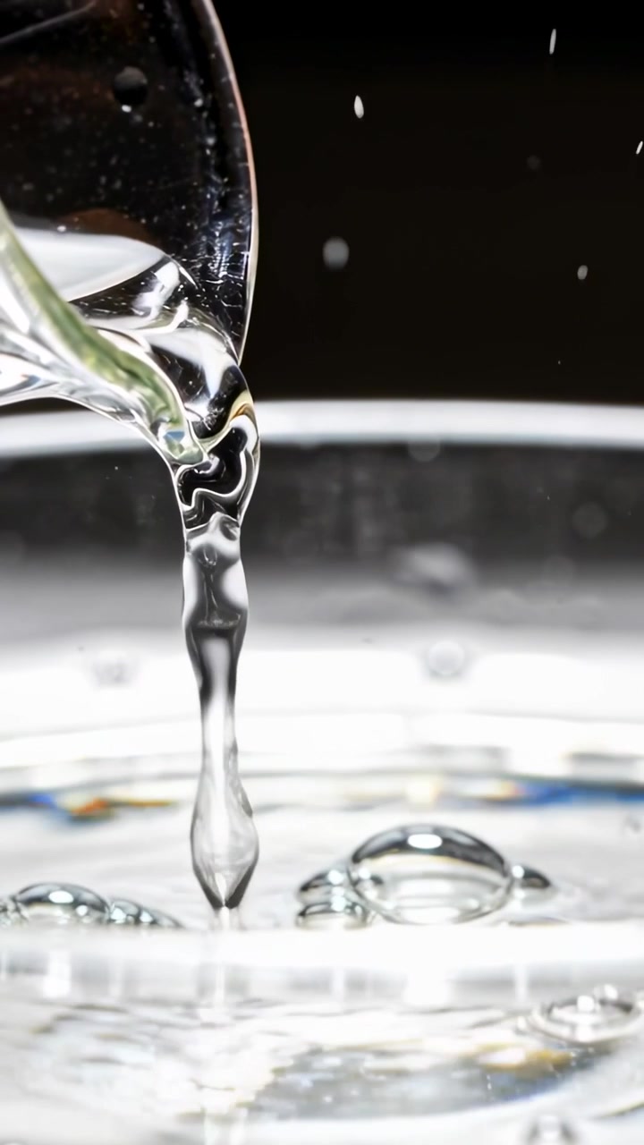 Video verticale: Recipiente che si inclina versando un getto limpido in una ciotola poco profonda, creando gocce e increspature