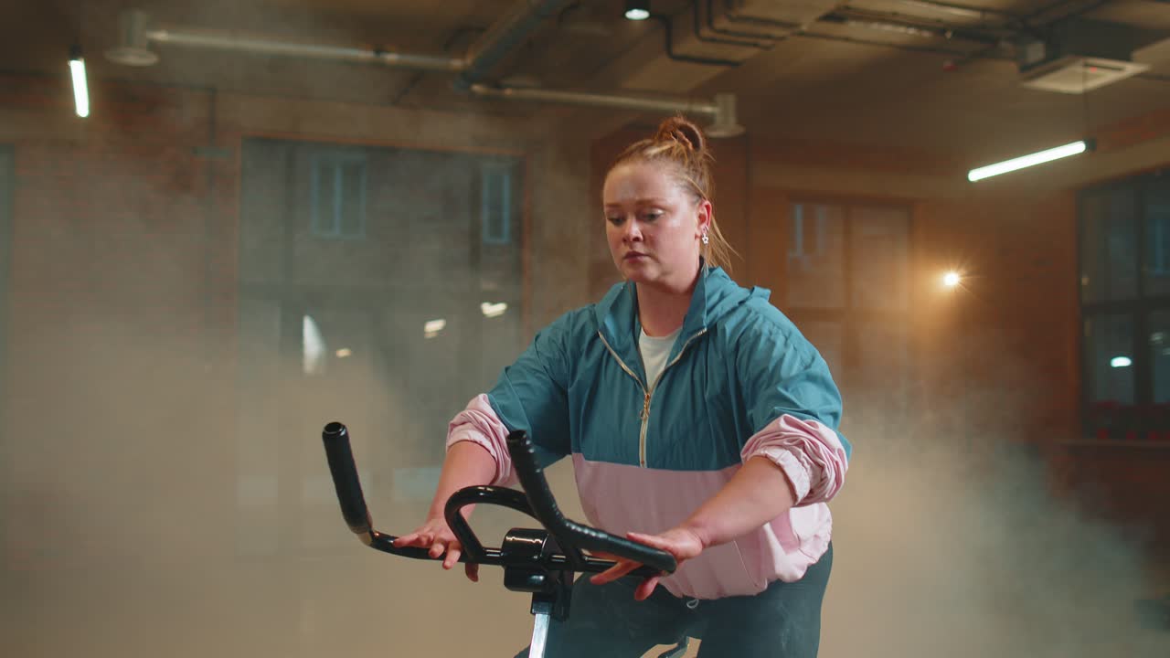 안개 가득한 체육관 에서 자전거 를 타고 에어로빅 라이딩 훈련 을 하는 운동 여자
