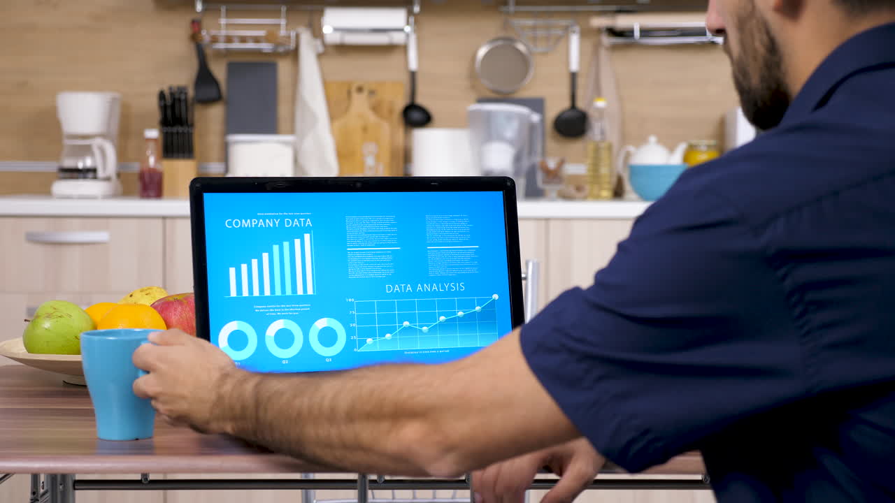 Man Analyzing Company Data on Laptop in Kitchen