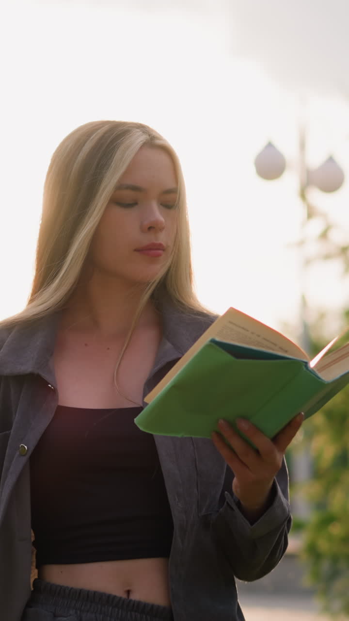joven dama caminando mientras lee un libro lo cierra pensativamente, mirando hacia otro lado mientras la luz del sol ilumina su entorno, el fondo presenta vegetación con luz suave y cálida y un borrón sutil