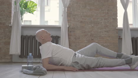 old man stretching and exercising on yoga mat at home 1