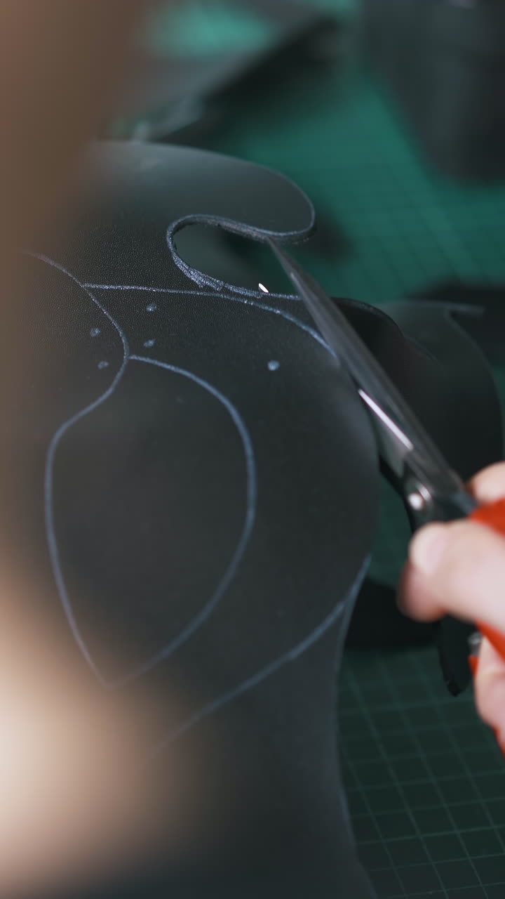 CU: Professional tailor cuts black leather mask template with large scissors at green cushion board extreme closeup