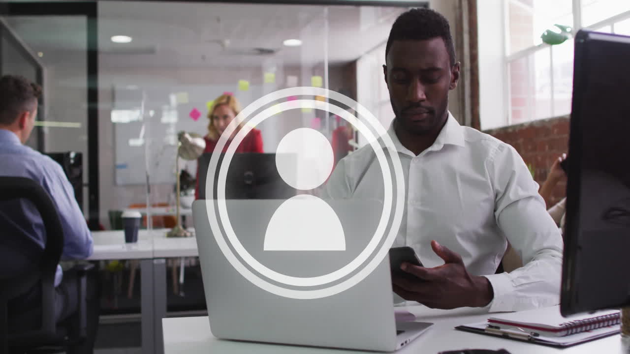 Man using smartphone and working on laptop in business office, showing floating charts and notes