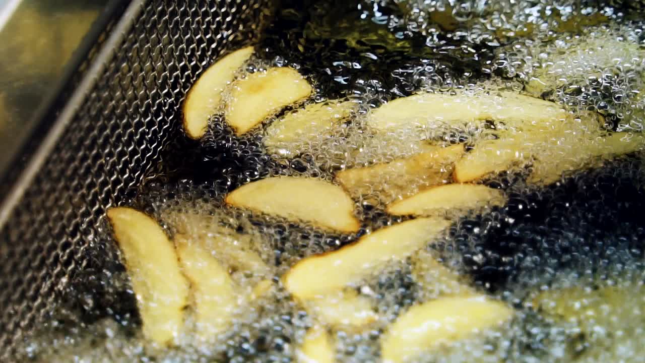 French fries are fried in boiling oil in a large container in the kitchen. Potato pieces in fat. Close-up slow motion