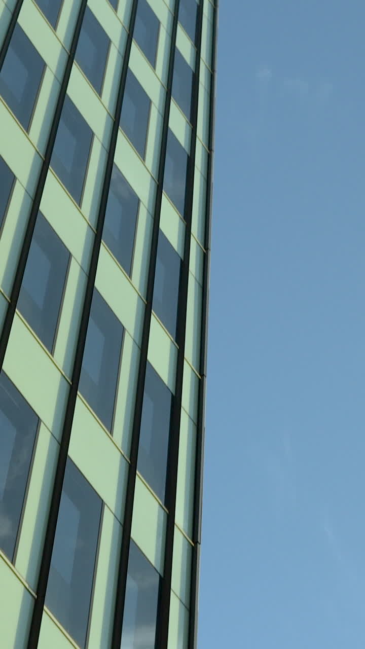 Una toma vertical de ángulo bajo de la fachada de un edificio de oficinas moderno con ventanas de cristal que reflejan el cielo azul. Ideal para contenido corporativo, inmobiliario y de desarrollo urbano.