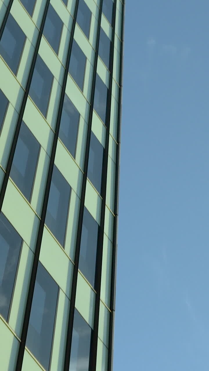 Un'inquadratura verticale dal basso di una moderna facciata di un edificio per uffici con finestre di vetro che riflettono il cielo blu. Ideale per contenuti aziendali, immobiliari e di sviluppo urbano