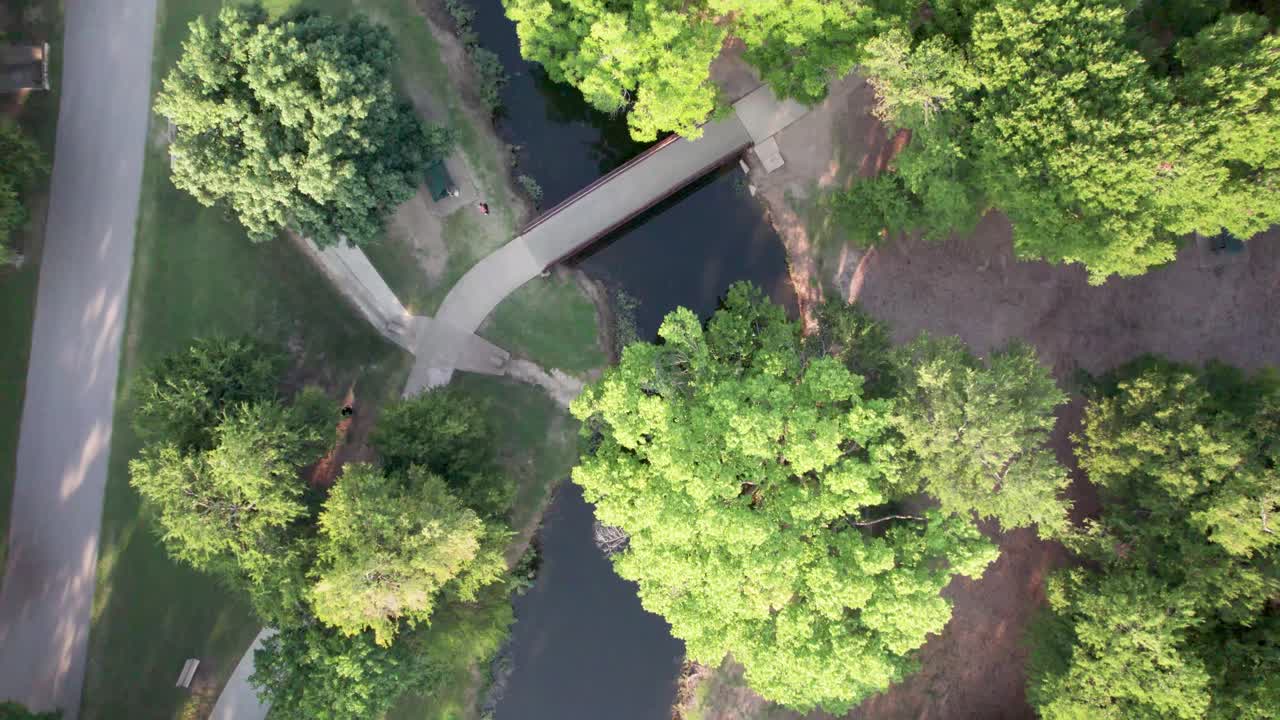 Aerial footage of Bear Creek Park in Keller, Texas. Camera is looking straight down, flying over the creek. People can be seen walking on the trail and a bridge going across the creek