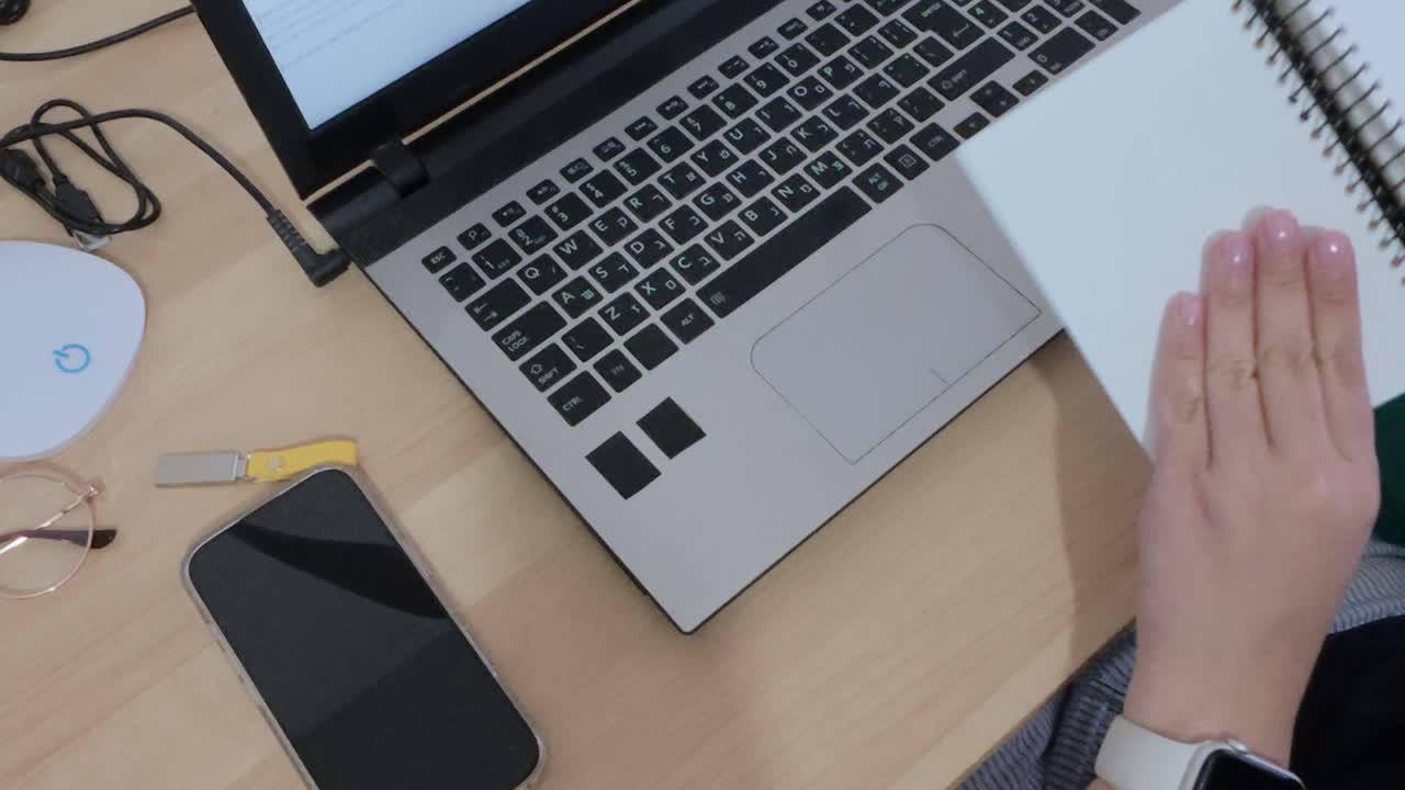 Person working remotely, writing notes in a spiral notebook while using a laptop. management.