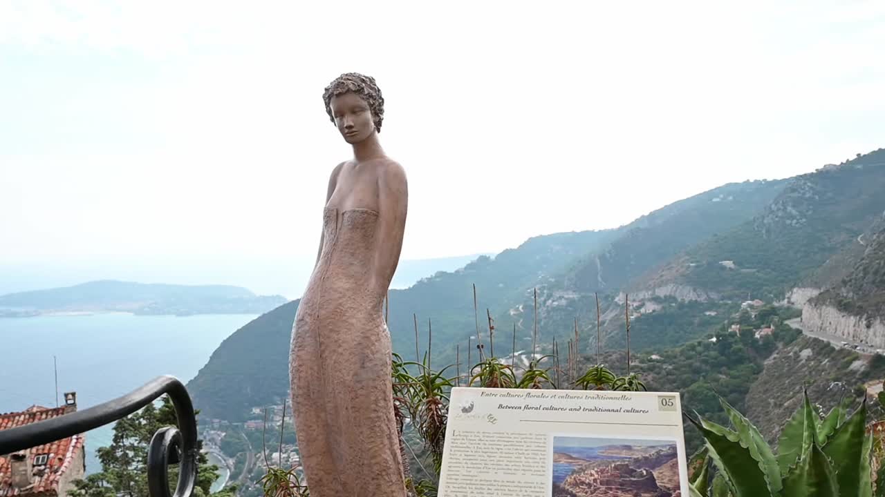 Statue and a sign in a park with tropical plants in Menton, France. Sea on the background