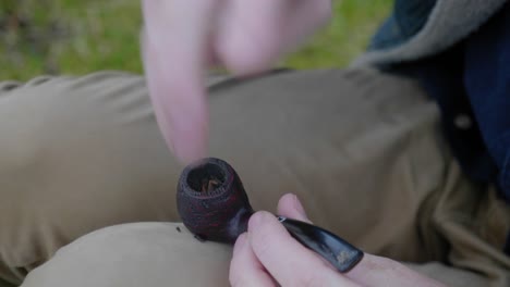 un primer plano de un hombre empacando el recipiente de una pipa con tabaco