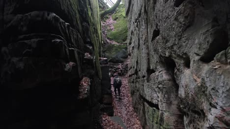 hombre caminando entre enormes formaciones rocosas en la ruta de senderismo mullerthal en luxemburgo - cámara en la espalda