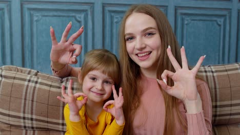 Portrait-of-little-child-kid-daughter-with-young-mother,-hugging,-embracing,-showing-ok-gesture-sign