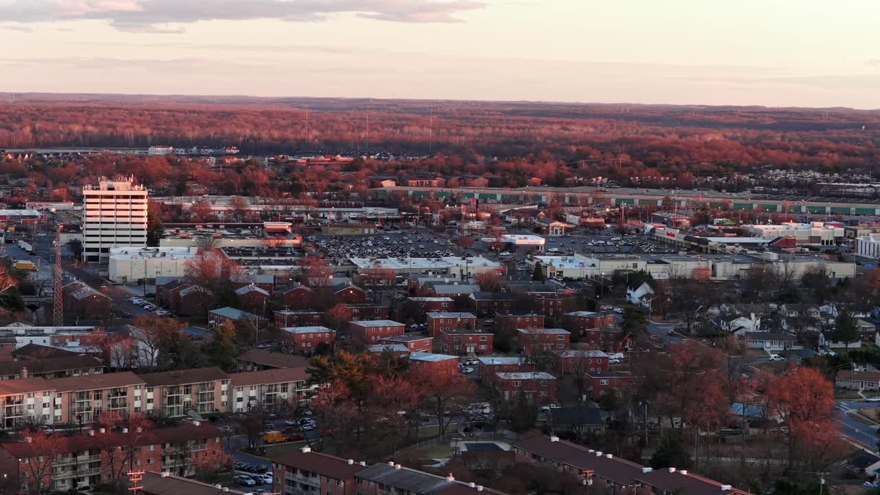 Luftfoto av Laurel, Pennsylvania ved solnedgang som viser boligblokker, næringsbygg og parkeringsområder omgitt av høstfargede trær under varmt kveldslys i en liten amerikansk by