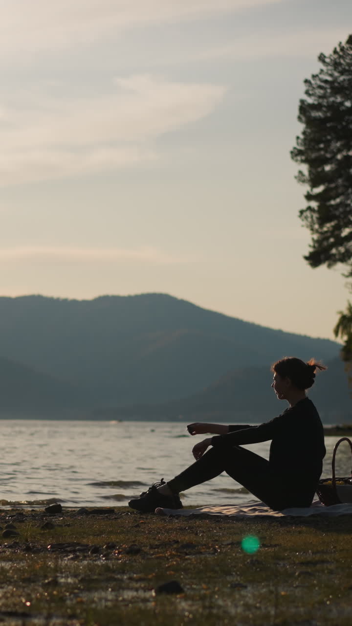 바위 돌을 호수에 던지는 여인: 음식 바구니를 들고 있는 여인이 해가 지면 강변에서 평온한 순간을 즐기며 시간을 보낸다.