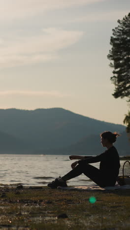 dama arrojando piedras de guijarros al lago. mujer con canasta de comida pasa el tiempo disfrutando de un momento de tranquilidad en la orilla del río al atardecer. fin de semana sola