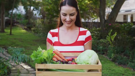 Mujer-Caucásica-Sonriente-De-Pie-En-El-Jardín-Sosteniendo-Una-Caja-De-Verduras