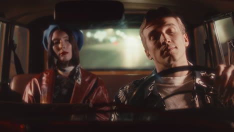 man driving vintage car at night with female passenger in back seat