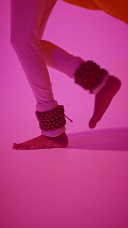 vertical video close up of feet with bells of female kathak dancer performing dance wearing traditional indian dress against purple background 4