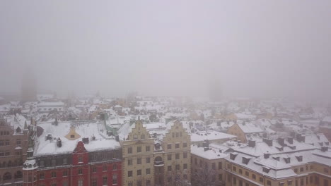 Low-altitude-pass-with-drone-over-the-Gamla-Stan-district-in-Stockholm-Sweden-on-a-snowy-foggy-day-with-views-of-the-German-Church
