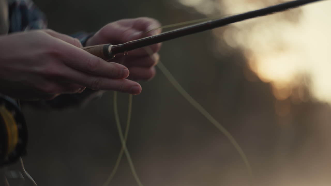 Person preparing fly fishing rod at sunset