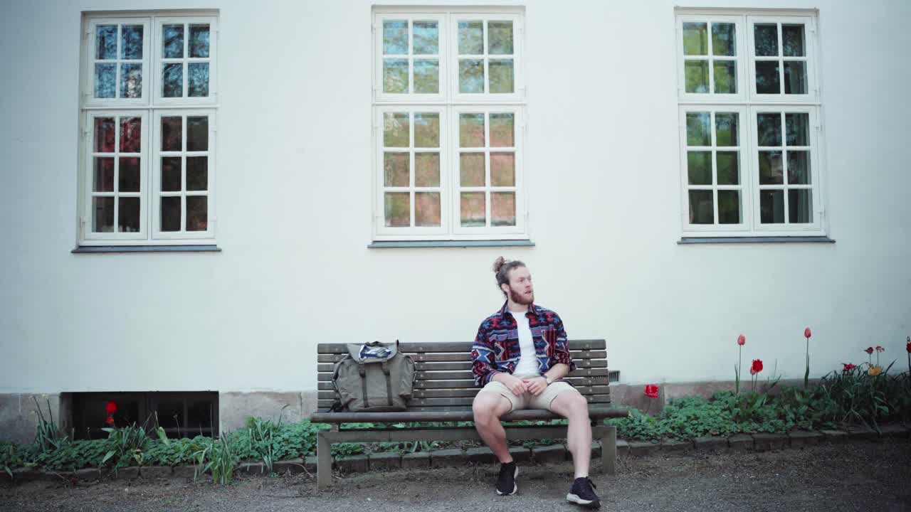 Adventurer taking a break on a bench in front of a white house looking around in copenhagen