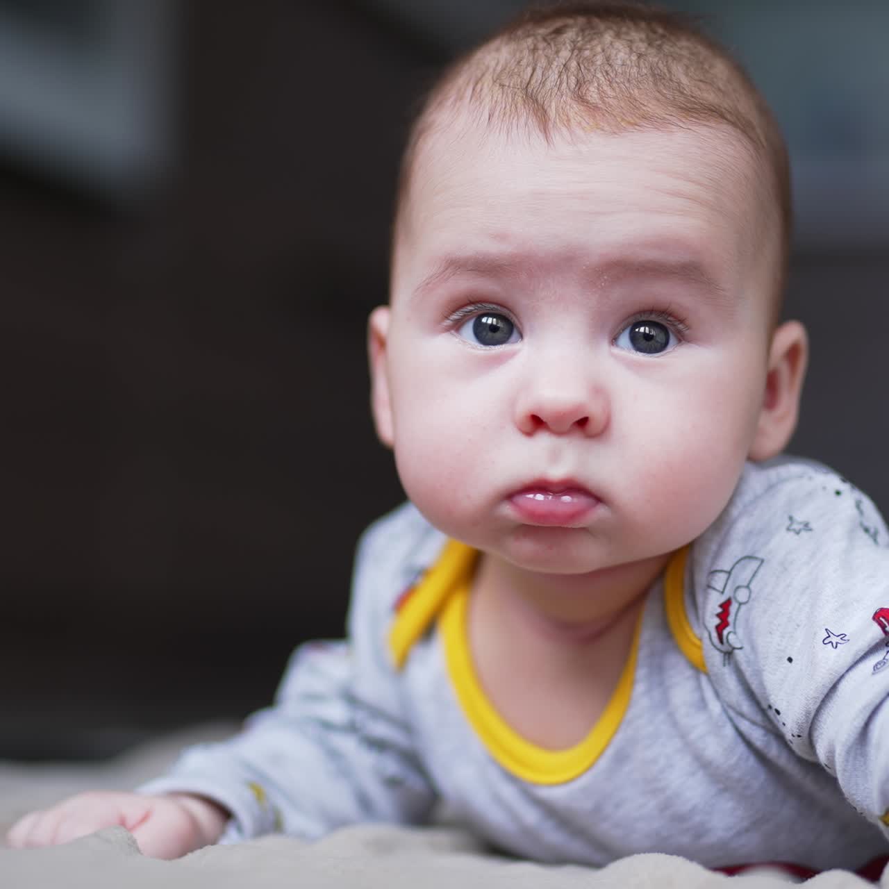 Beautiful Caucasian child lies on his tummy holding head up high. Curious little boy looks sideways with eyes wide open. Close up