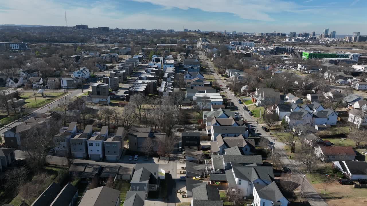 Vista aerea invernale di un quartiere residenziale di Nashville con file di case unifamiliari, strade suburbane e skyline del centro visibile in lontananza sotto la luce chiara del giorno. Luce solare a gennaio.