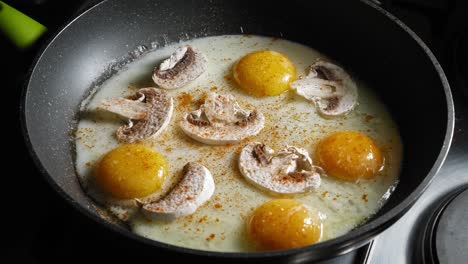 frying eggs with champignon mushrooms in a pan, seasoned with salt, pepper, and cayenne powder