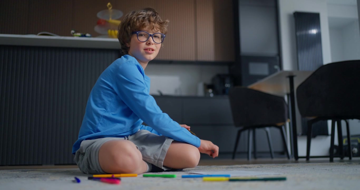 Ragazzo concentrato con gli occhiali che colora su carta a casa