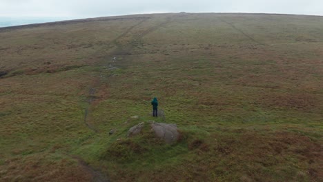 tomada giratoria de un dron de un turista de pie en una roca y experimentando la belleza de los campos en cinco piedras en inglaterra