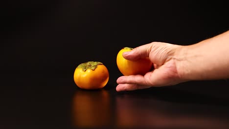 a hand reaches for two persimmons