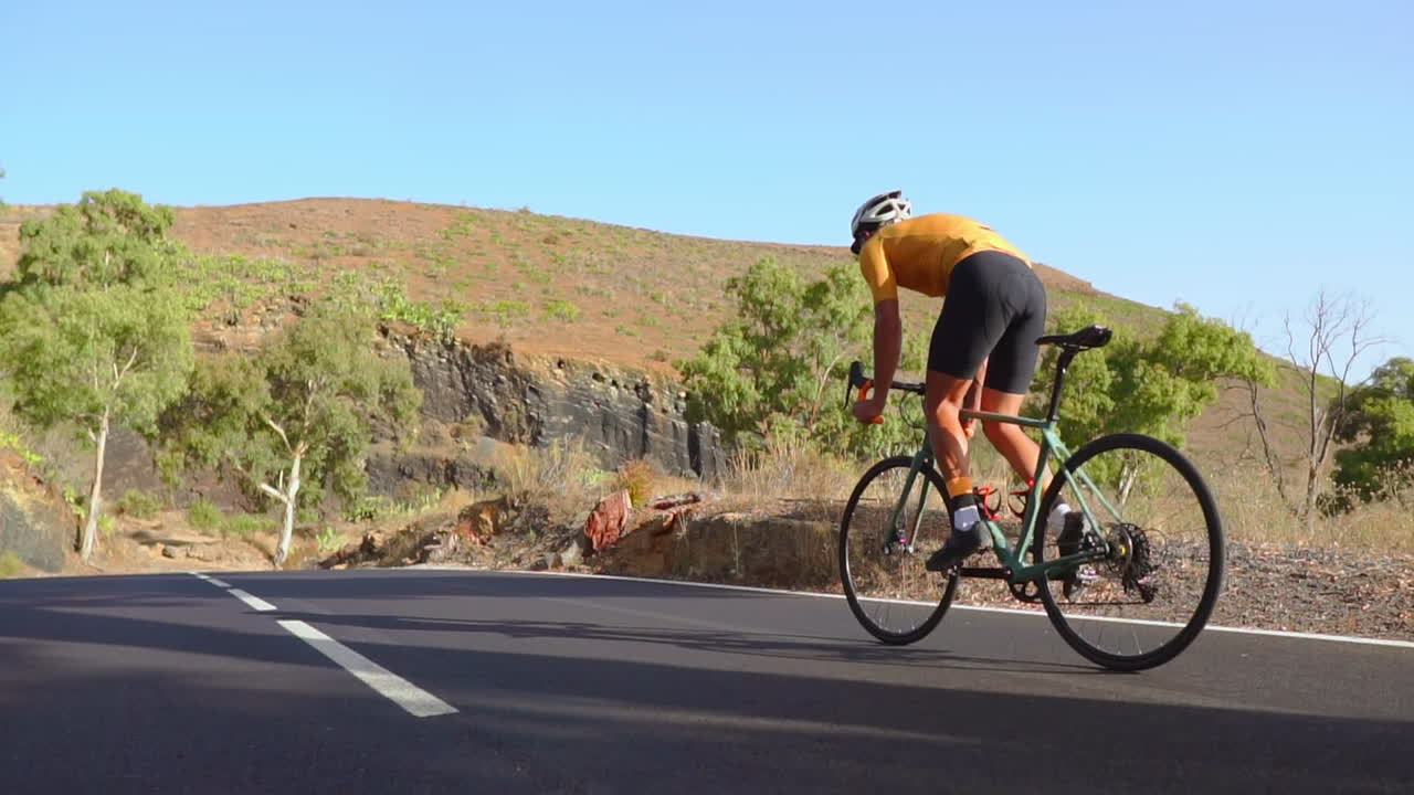 Embracing the tranquility of the morning, a man cycles on a road bike along an unoccupied road. The slow-motion video amplifies the concept of extreme sports