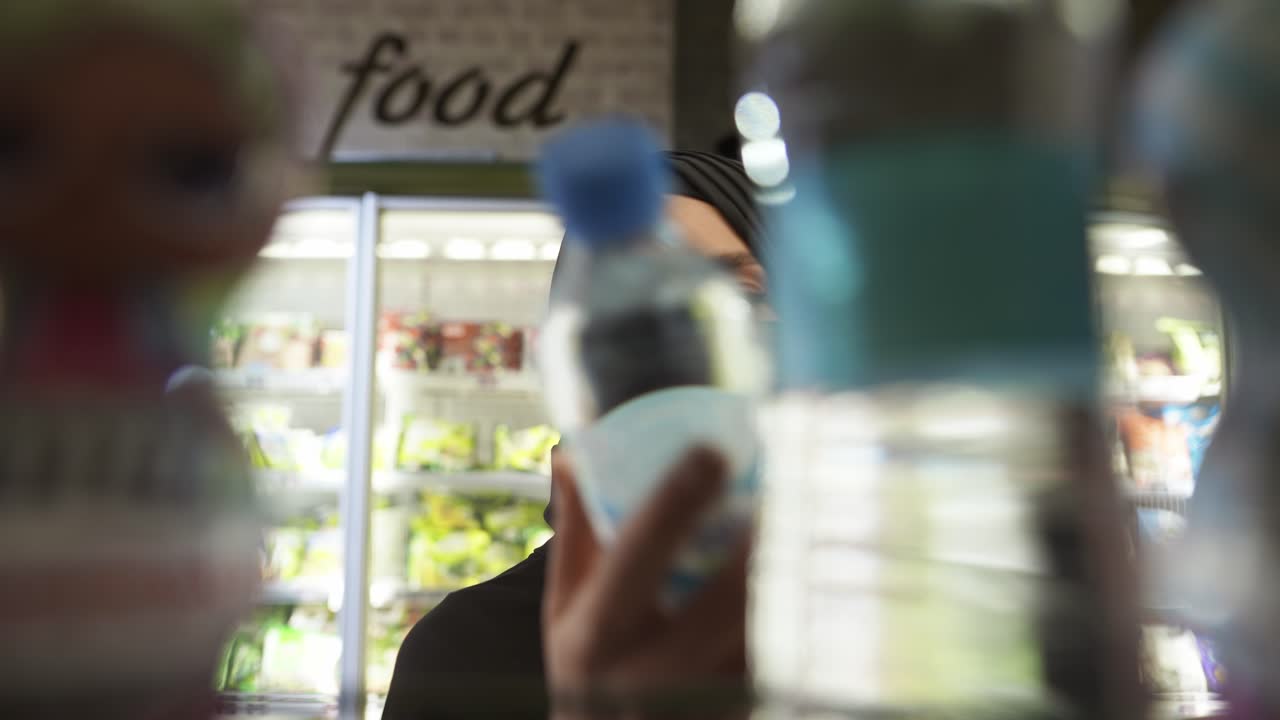 히자브와 보호 마스크를 입은 여성 선반에서 물 병, 내부의 영상