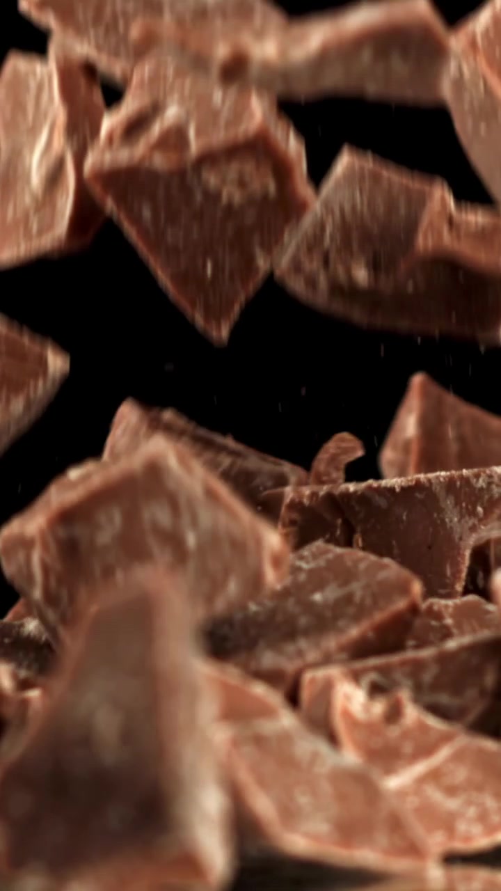 Pezzi di cioccolato al latte che cadono al rallentatore su sfondo nero