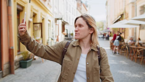 Mujer-Bloguera-Tomándose-Un-Selfie-Con-Un-Teléfono-Inteligente-Y-Comunicándose-Mediante-Videollamada-En-Línea-Con-Sus-Suscriptores-En-La-Ciudad