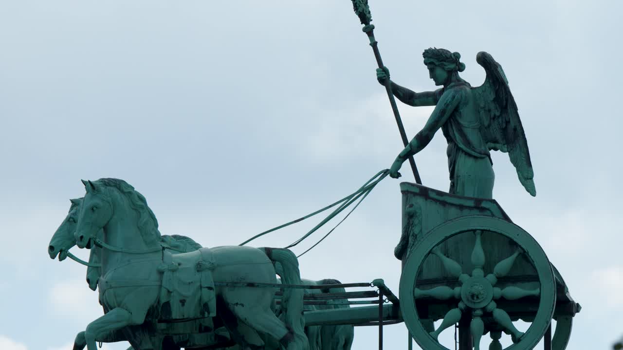 Camera pans left across quadriga statue silhouette against cloudy sky, soft daylight, Berlin, Germany