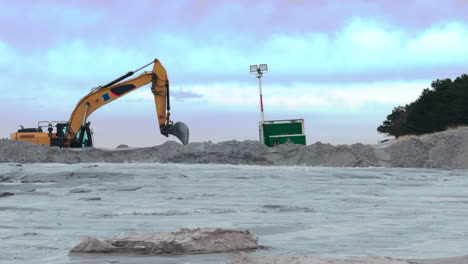 a large excavator shovels sand that has been washed up from the baltic sea to repair the beach