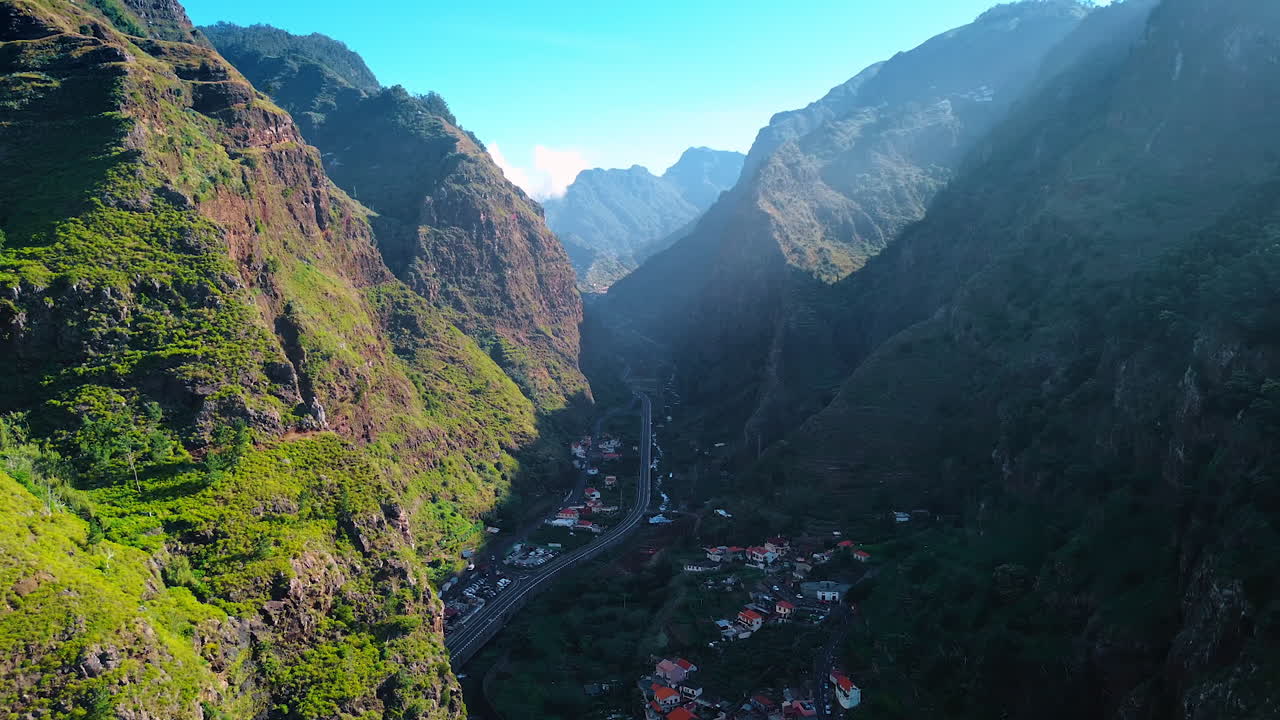 Highway crosses the town located between two high mountains. One rock is still lit with bright sun when another one is shading the town. The Madeira Islands, Portugal. Top view.