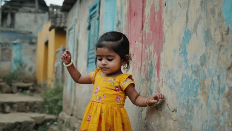 adorable toddler girl wearing a yellow dress leaning against a weathered, vibrantly colored wall in a developing nation, capturing the essence of childhood resilience and cultural diversity