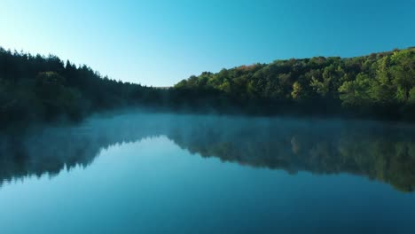 early morning low drone shot over glossy lake with some fog-1