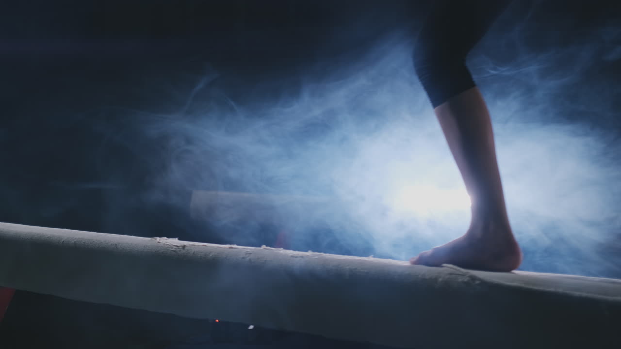 Close-up of the foot of a professional gymnast girl jumping in slow motion in the smoke on a balance beam. Women's gymnastics. Grace and a healthy lifestyle