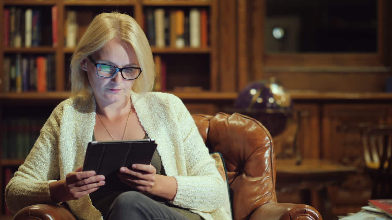 A Woman Reads A Book In A Tablet Sits In The Luxurious Back Of The Library