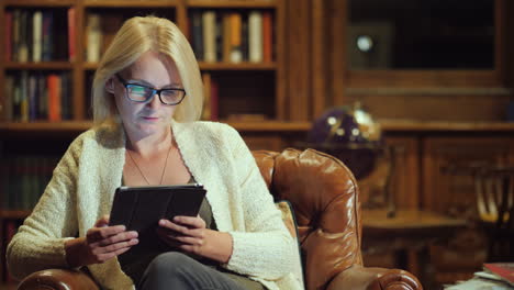 a woman reads a book in a tablet sits in the luxurious back of the library