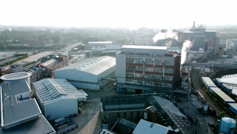 industrial warehouse building making steam emissions aerial view across canal railway in early morning sunlight