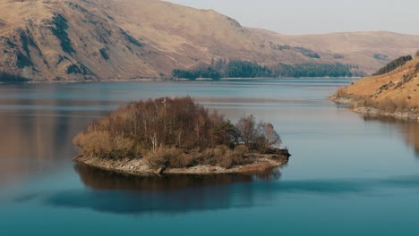 drone slowly descends panning up to reveal lake and tree-covered hills in early spring