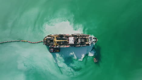 wide top down aerial footage of a ship that is dredging up sand in the harbor of bari, italy