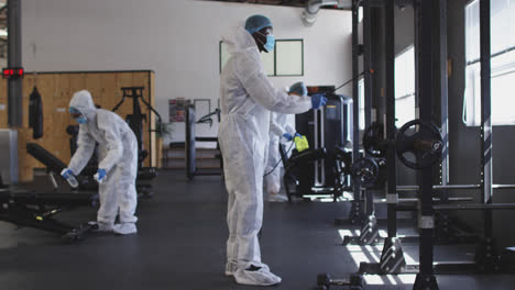 equipo de trabajadores de la salud con ropa de protección limpiando el gimnasio con un pulverizador desinfectante