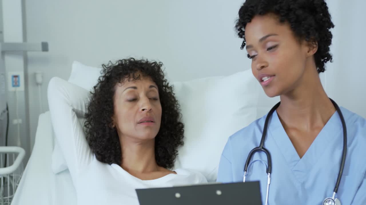 Front view of African american female doctor talking with female patient in the ward at hospital