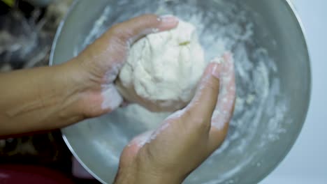 close up view of african american woman's hands kneading pizza dough in a silver pan in slow motion